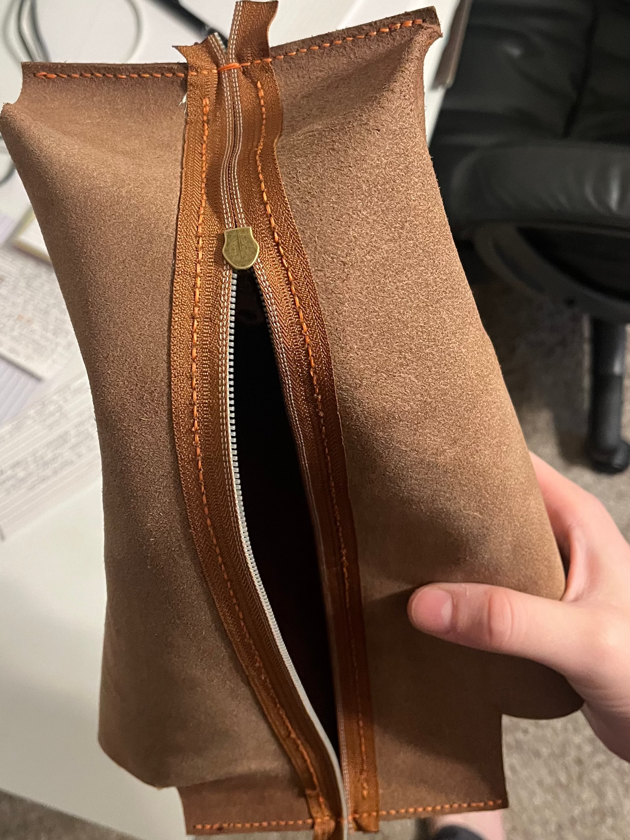 Brown leather pouch held by a hand in an office setting